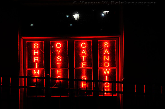 New Orleans night scene of red neon lights, offering shrimp, oysters, catfish and sandwiches.