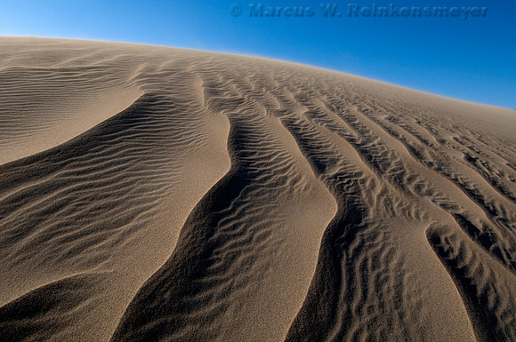 Sand dune ripples and clear blue skies at Mesquite Flats Dunes, a large expanse of sand near Stove Pipe Well, Death Valley National Park, California.
